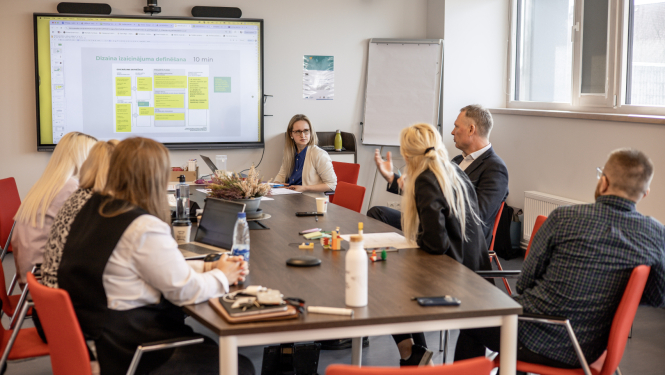 Inovāciju sprints - dalībnieki sēž pie galda, sarunājas un vēro ekrānu