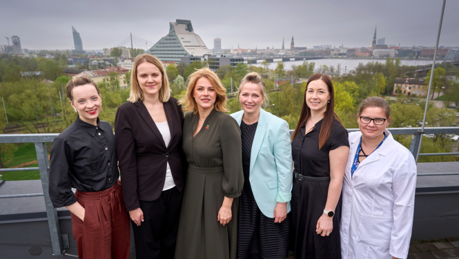 Ministru prezidente Evika Siliņa kopā ar Latvijas jaunajām zinātniecēm uz Latvijas Universitātes Zinātņu mājas jumta, fonā Latvijas Nacionālās bibliotēkas ēka un skats uz Rīgas panorāmu  