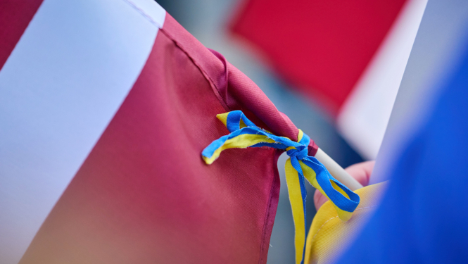 Latvijas karogs, kuram ap kātu apsieta lentīte Ukrainas karoga krāsās