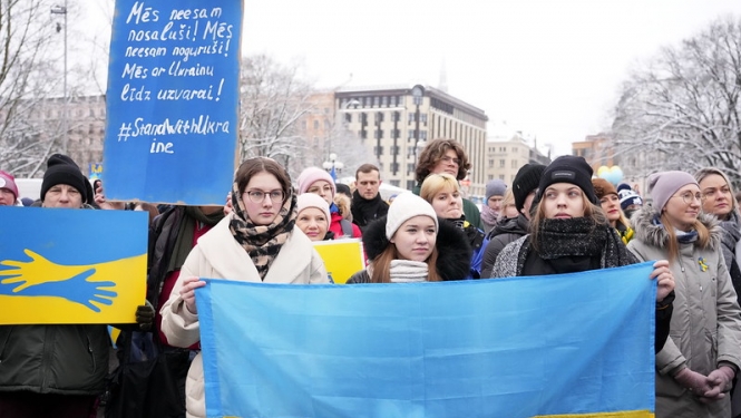 Ukrainas atbalstam sapulcējušies cilvēki ar Ukrainas karogiem, plakātiem Ukrainas atbalstam pie Brīvības pieminekļa