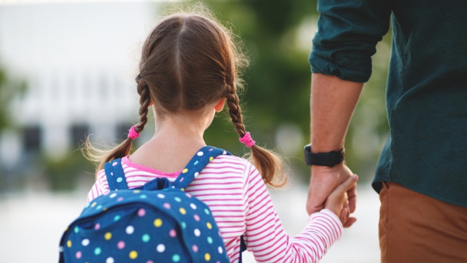 Meitenīte ar skolas somu tur roku tētim