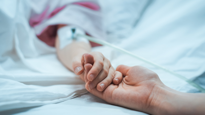 Vecāks tur slimnīcas gultā guloša bērna roku