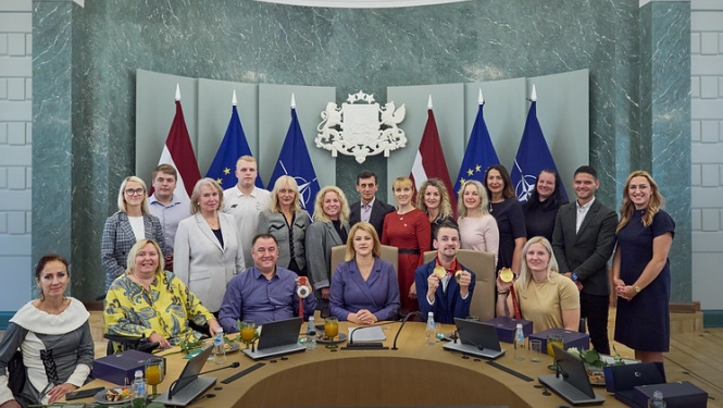 Kopbilde MK sēžu zālē, kurā redzami Latvijas paraolimpieši, treneri, delegācijas dalībnieki un centrā Ministru prezidente. 