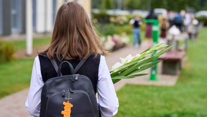 Skolniece ar melnu mugursomu no mugurpuses, rokās baltas gladiolas