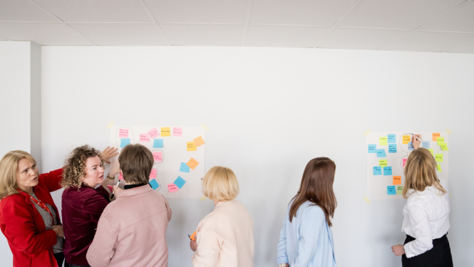 Inovāciju sprints - cilvēki pēta pie sienas piespraustas krāsainas līmlapiņas