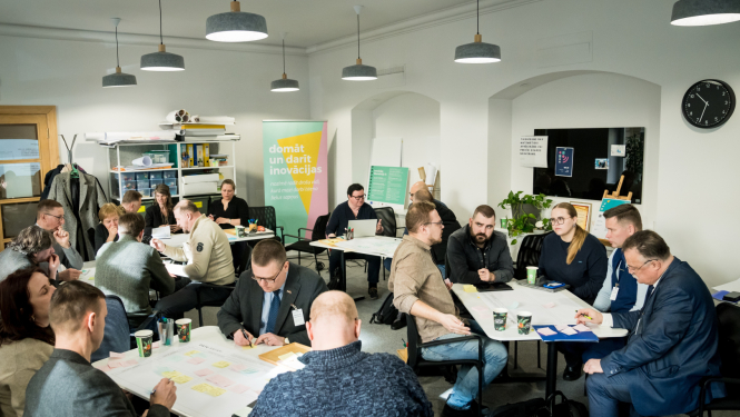 Inovācijas sprints - cilvēki sēž pie galdiņiem, sarunājas