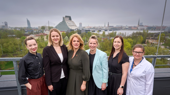 Ministru prezidente Evika Siliņa kopā ar Latvijas jaunajām zinātniecēm uz Latvijas Universitātes Zinātņu mājas jumta, fonā Latvijas Nacionālās bibliotēkas ēka un skats uz Rīgas panorāmu  