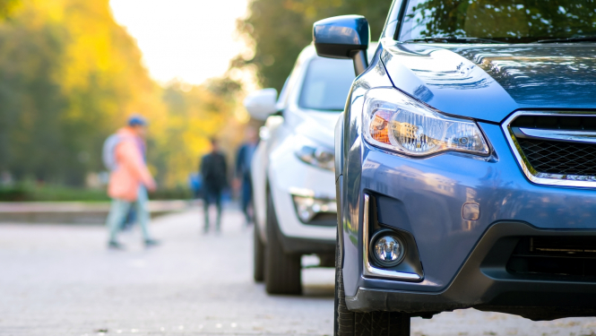 2 auto uz ielas. Fonā koki, cilvēki