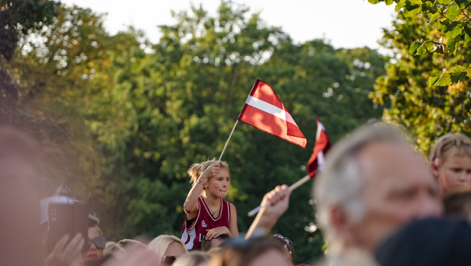 Basketbolistu sagaidīšana pie Brīvības pieminekļa. Meitene tur rokās Latvijas karogu. 