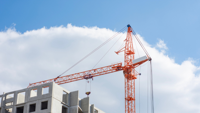 Oranžs ceļamkrāns pie jaunbūvējamas ēkas konstrukcijas