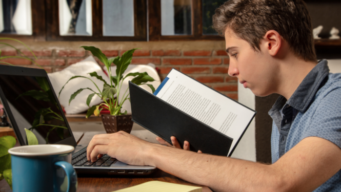 Skolēns pie datora lasa grāmatu