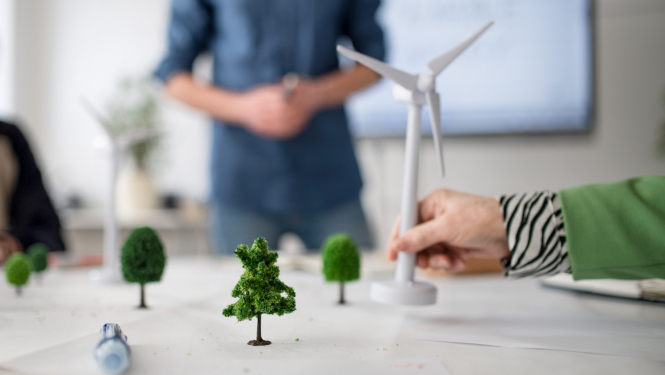 Attēlā redzama darba grupa vai sanāksme, kurā cilvēki apspriež klimata pārmaiņu risinājumus, izmantojot vizuālu maketu.
