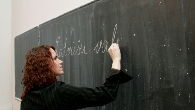 Sieviete raksta uz tāfeles latviešu valodā