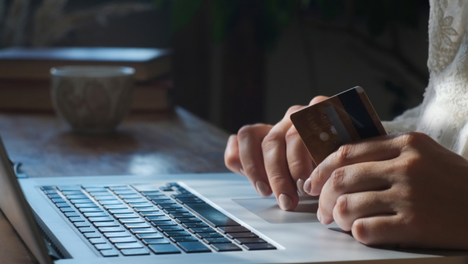 Cilvēks norēķinās ar karti internetā. 1 rokā tur kredītkarti. 