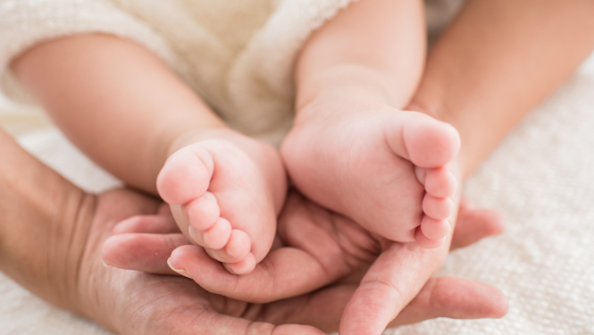 Pieaugušais tur rokās zīdaiņa kājas