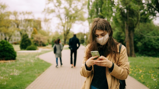 Meitene ar sejas masku skatās telefonā