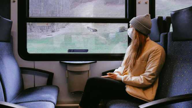 Meitene ar masku sēž vilcienā