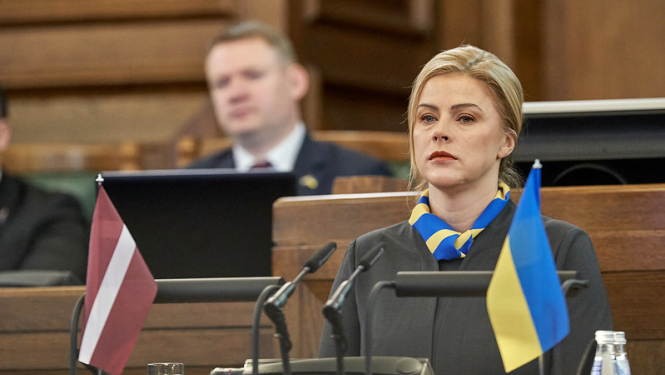 Ministru prezidente Evika Siliņa Saeimas sēdē. Uz tribīnes Ukrainas un Latvijas karogi. 