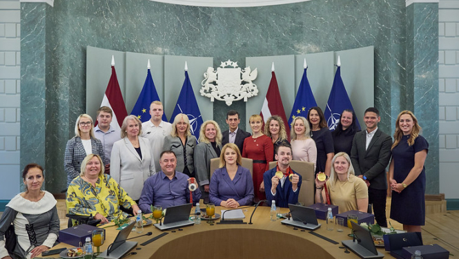 Kopbilde MK sēžu zālē, kurā redzami Latvijas paraolimpieši, treneri, delegācijas dalībnieki un centrā Ministru prezidente. 
