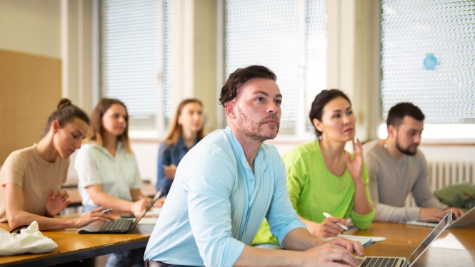Pieaugušo izglītība - cilvēki mācību telpā ar datoriem. 