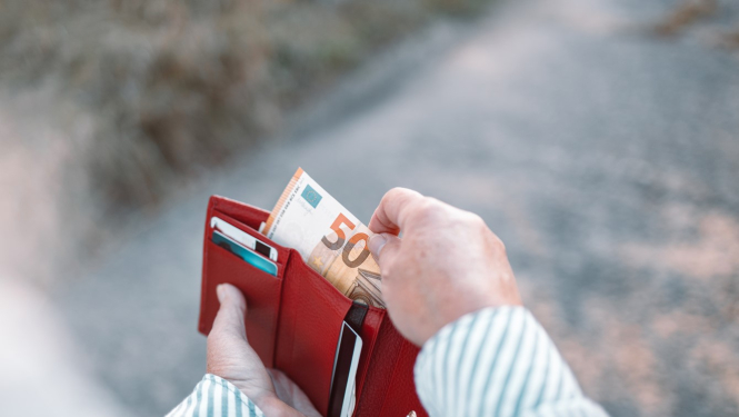 Tuvplānā sievietes rokas ar maku, kurā ir nauda