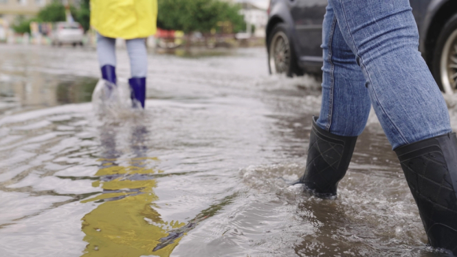 Cilvēki staigā gumijas zābakos ūdenī