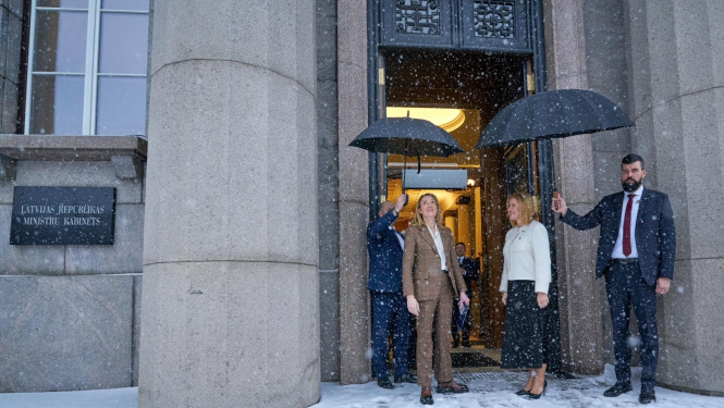 Roberta Metsola un Evika Siliņa pie valdības nama. Snieg sniegs un 2 vīrieši tur virs viņām lietussargus. 
