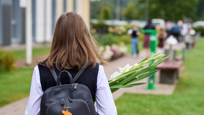 Skolniece ar melnu mugursomu no mugurpuses, rokās baltas gladiolas