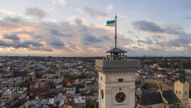 Skats no putna lidojumu pār Ukrainas pilsētu Ļvivu. Pirmajā plānā redzams pulksteņa tornis ar plīvojošu Ukrainas karogu