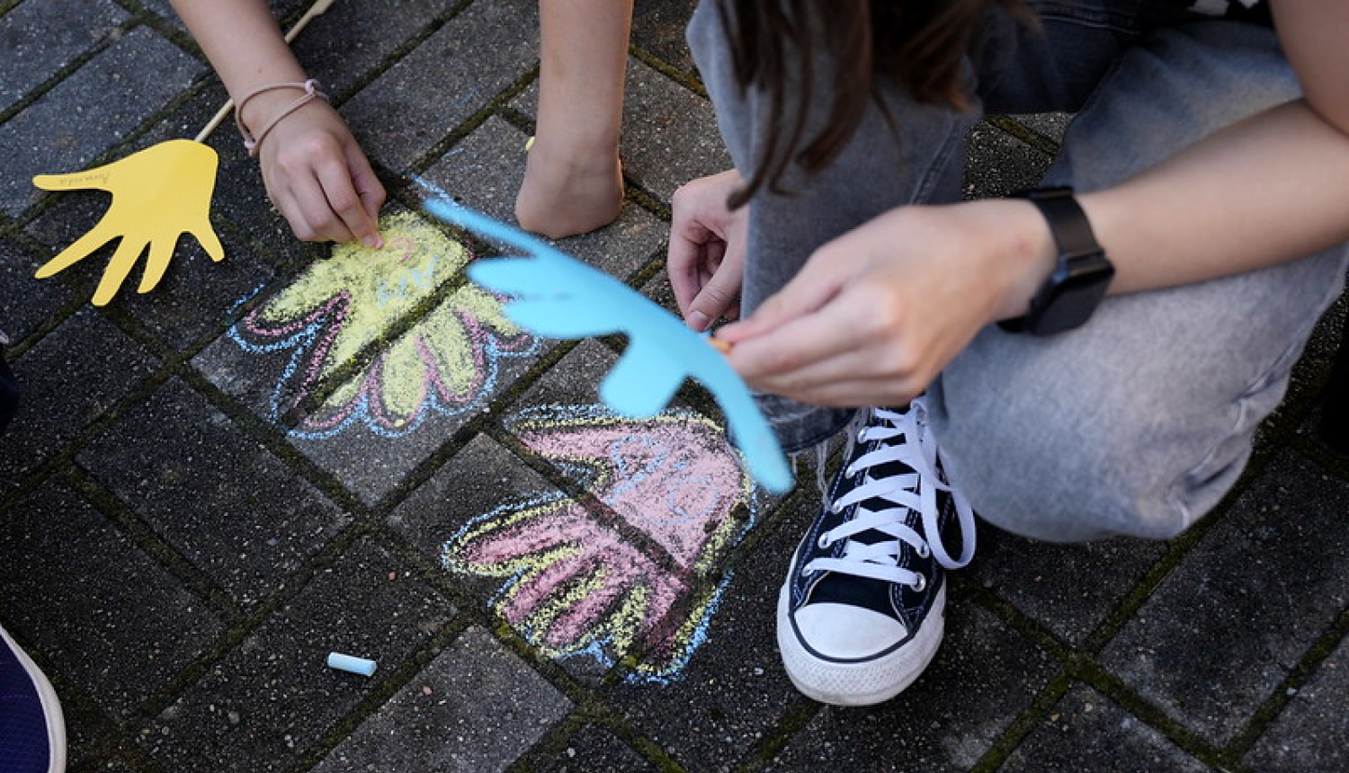 Bērni, kas ar krītiņiem uz bruģa zīmē rociņas krāsainas
