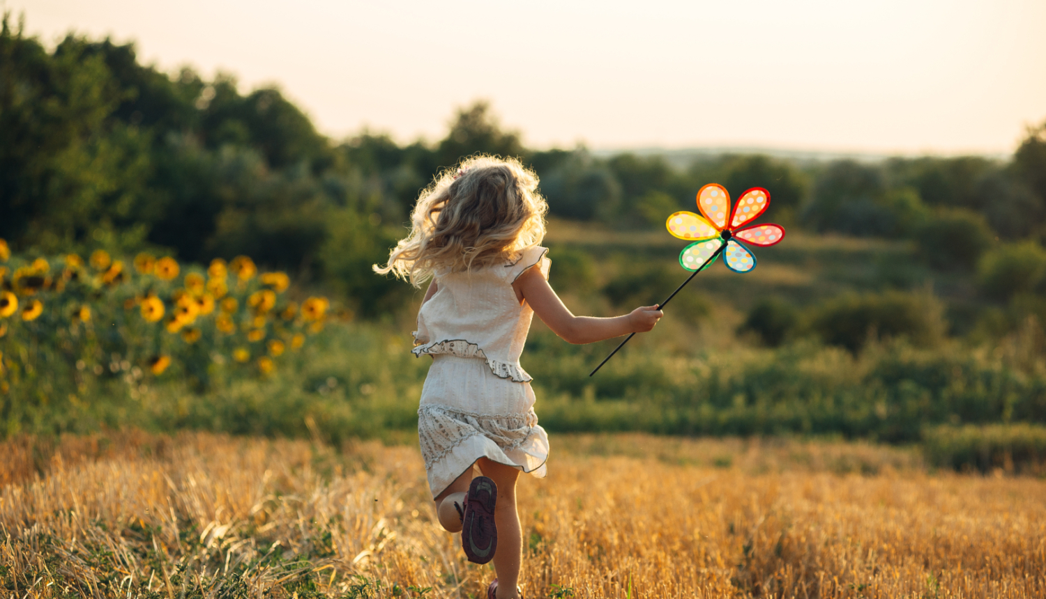 Bērns skrien pļavā, rokā krāsainas vējdzirnavas puķes formā