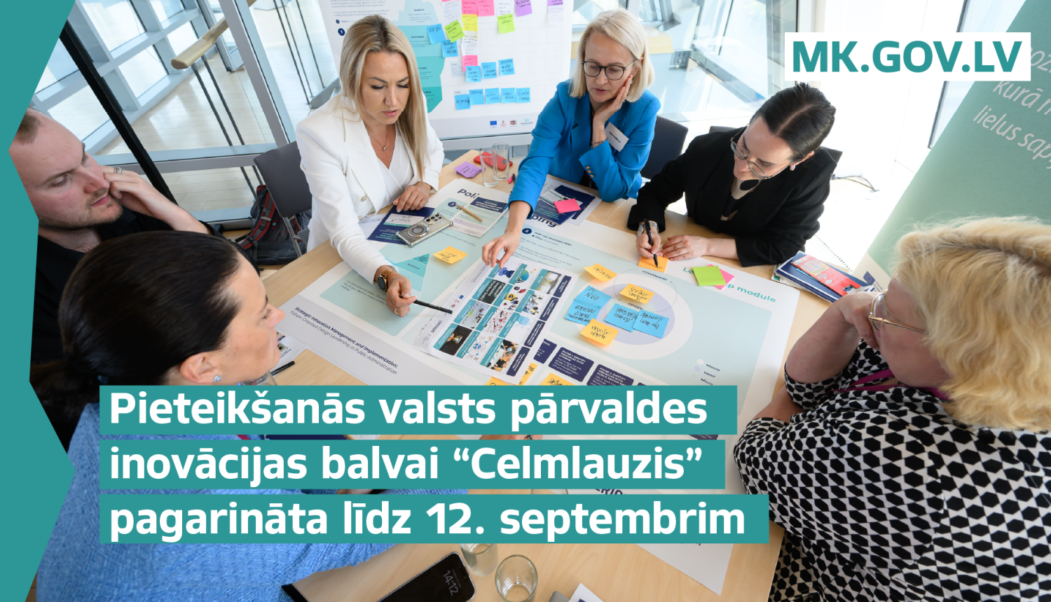 Cilvēki sēž ap galdu, apspriež uz galda redzamos dokumentus, materiālus