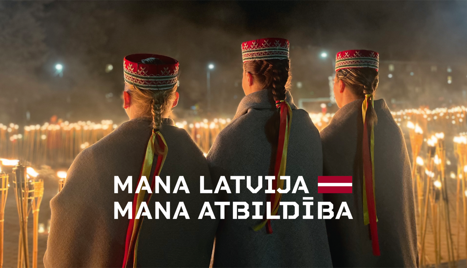 Trīs jaunas sievietes latviešu tautastērpos stāv pie pretī iedegtām lapām. Uz attēla sauklis - Mana Latvija, mana atbildība un Latvijas karoga grafisks atveids.