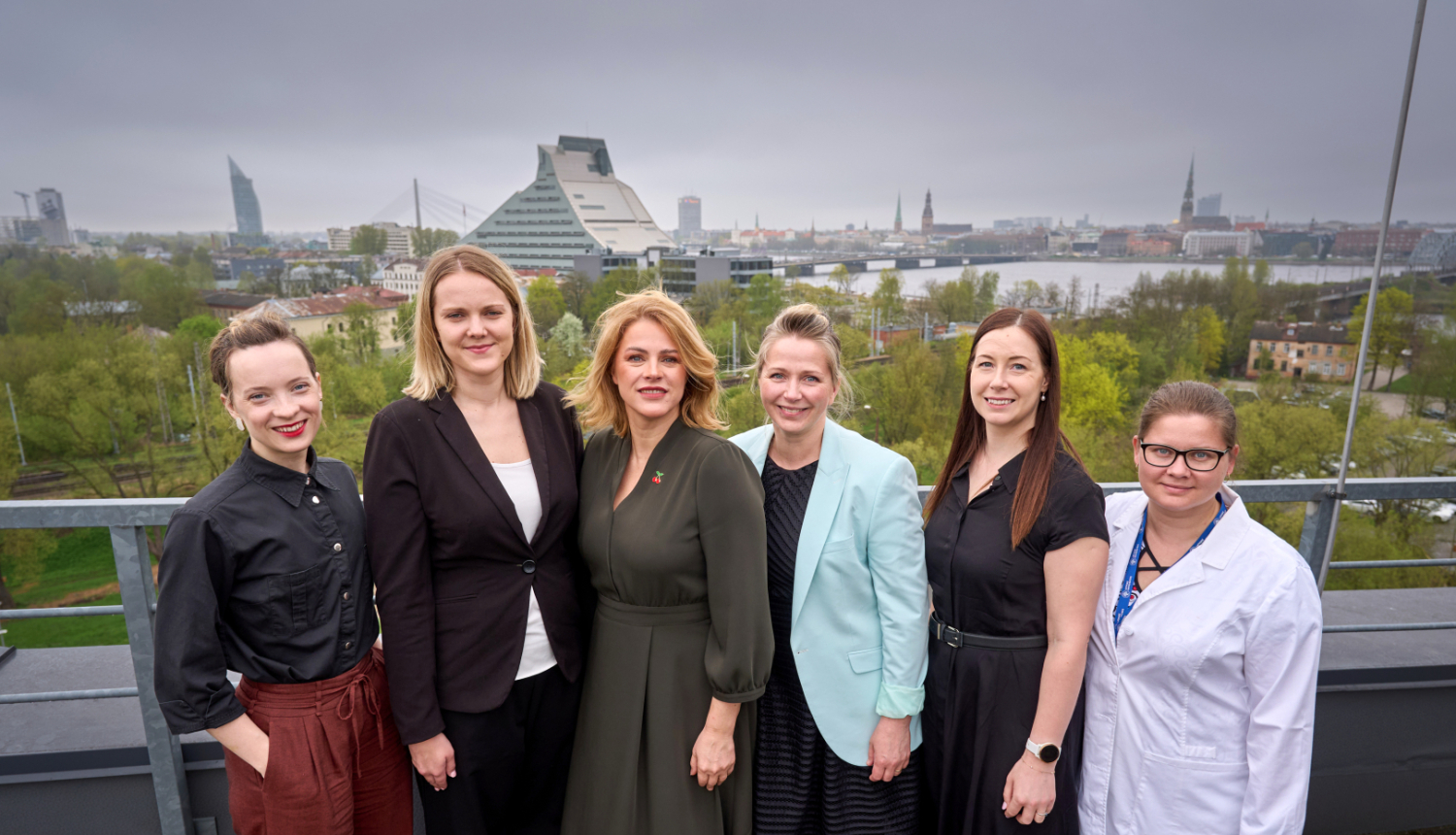 Ministru prezidente Evika Siliņa kopā ar Latvijas jaunajām zinātniecēm uz Latvijas Universitātes Zinātņu mājas jumta, fonā Latvijas Nacionālās bibliotēkas ēka un skats uz Rīgas panorāmu  