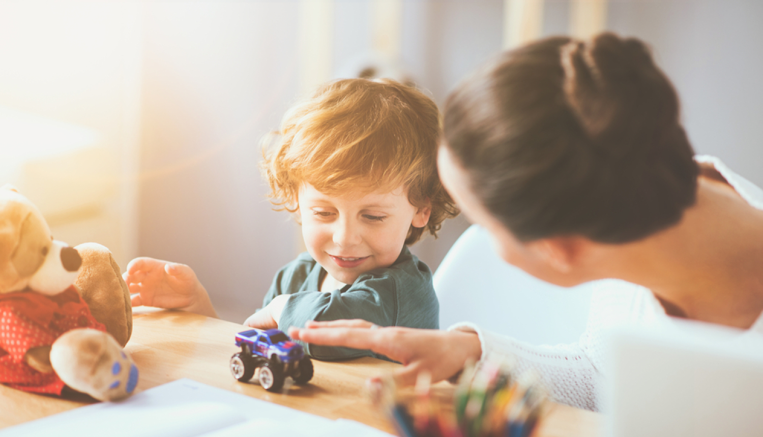 Bērns rotaļājas ar sievieti. Uz galda bērnu mantas. 