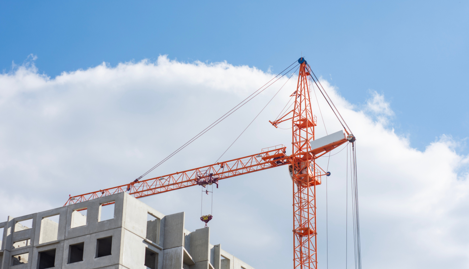 Oranžs ceļamkrāns pie jaunbūvējamas ēkas konstrukcijas