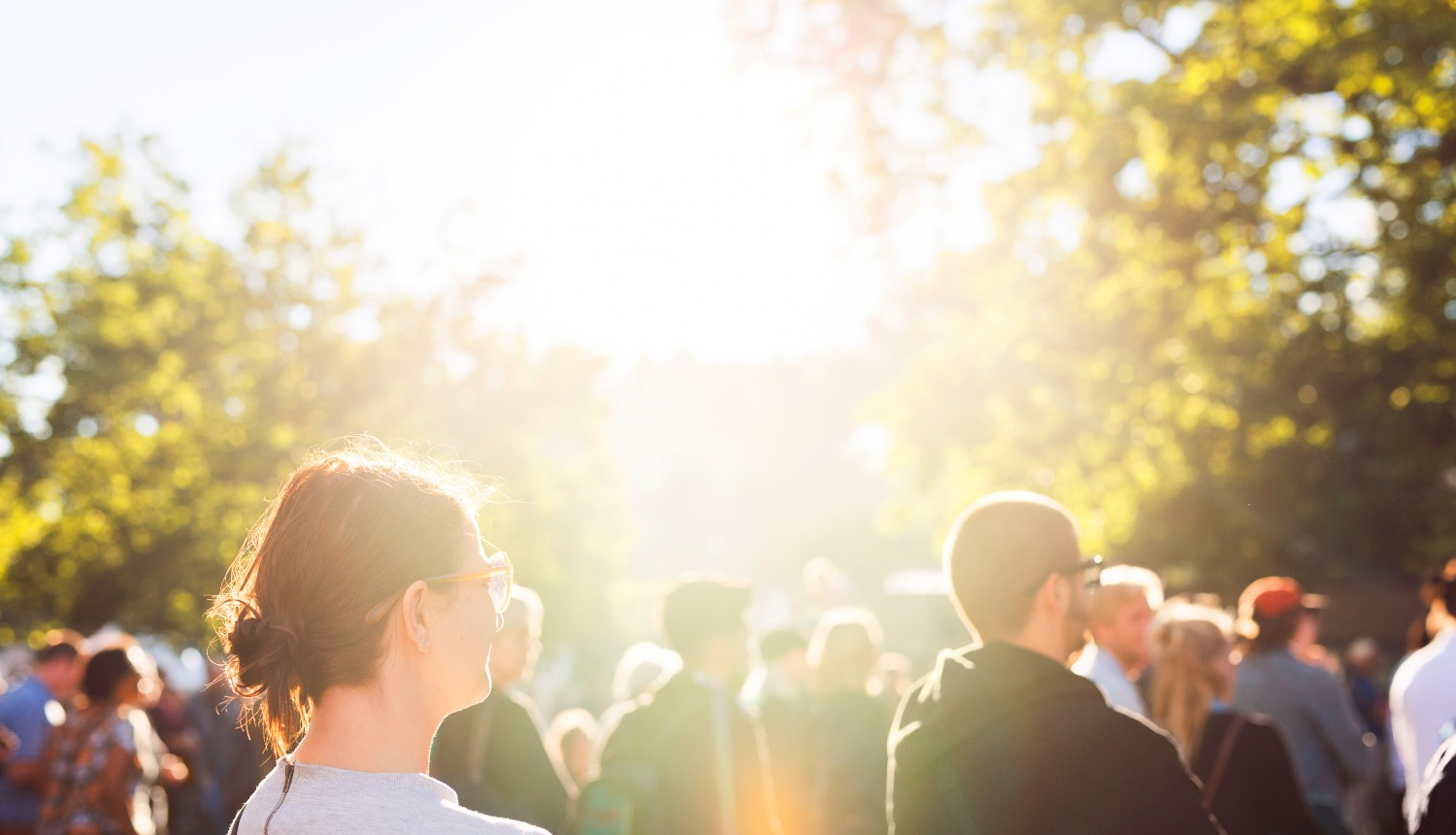 Sapulcējušies cilvēki brīvā dabā, viņus apspīd saules stari