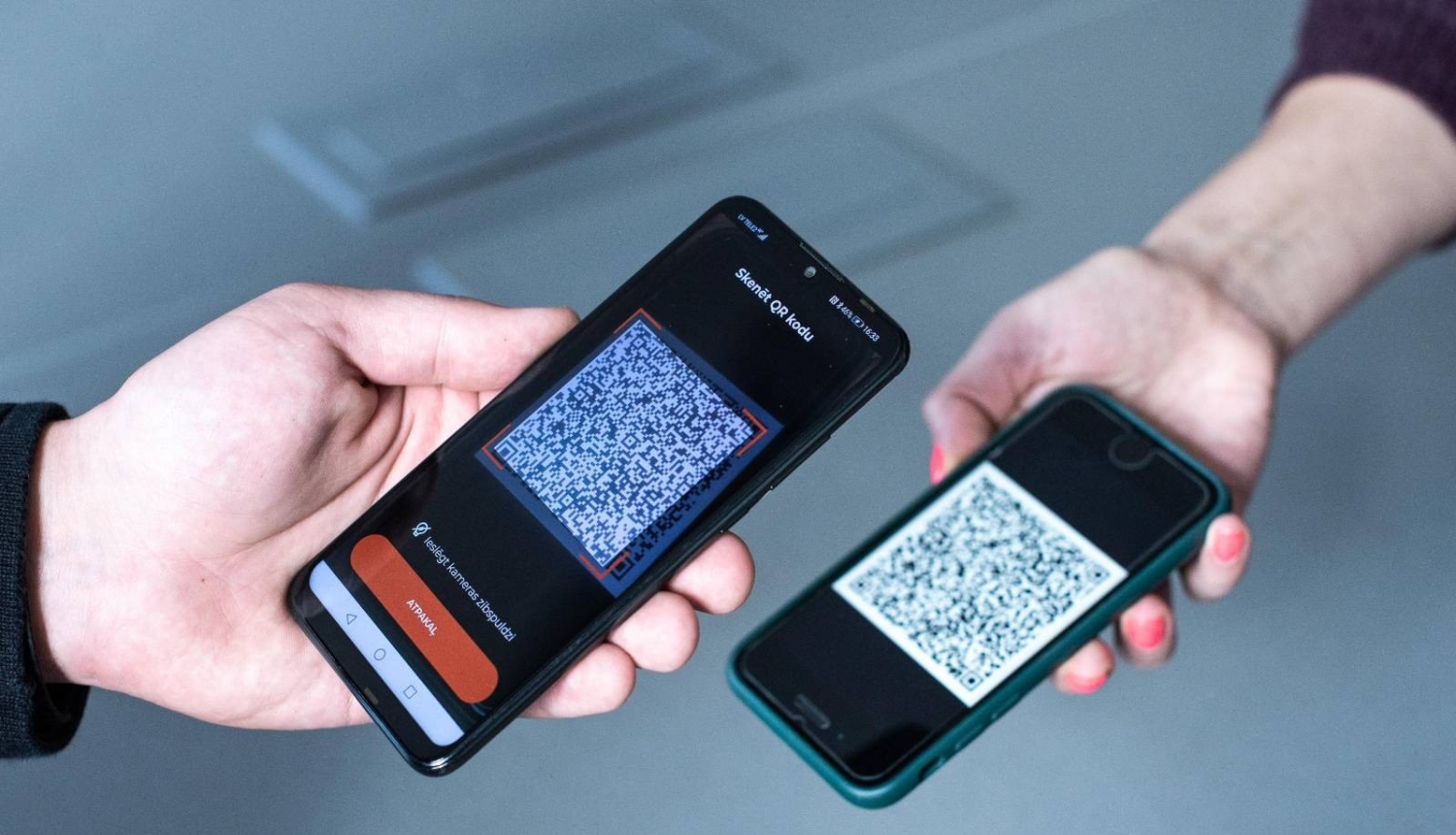Attēls: divi telefoni, notiek Covid-19 sertifikāta skenēšana
