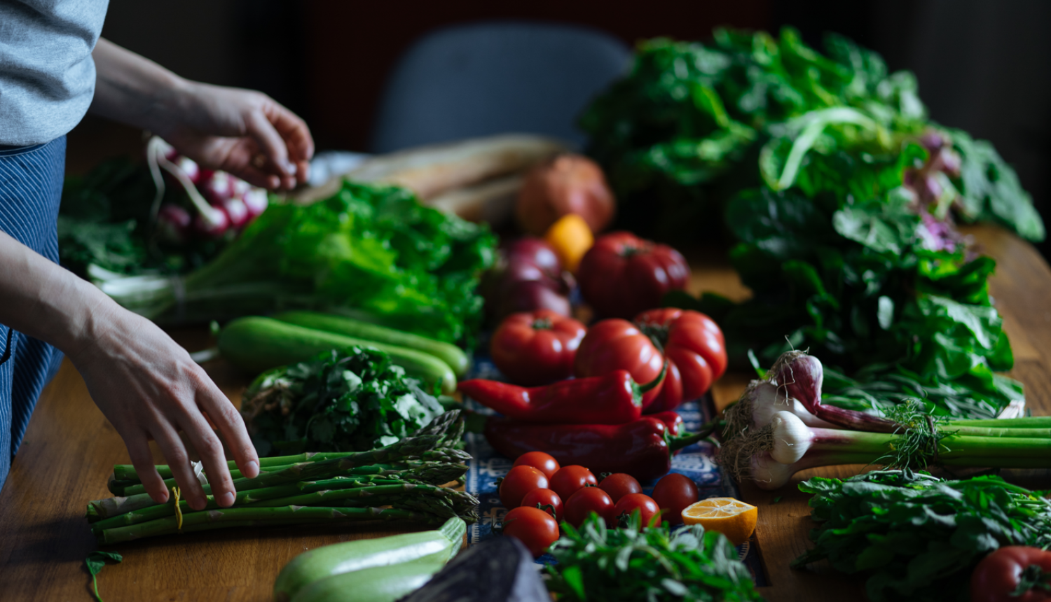 Dārzeņi (zaļumi, paprika, tomāti, kabači u.c. ) uz galda. Pie galda cilvēks.