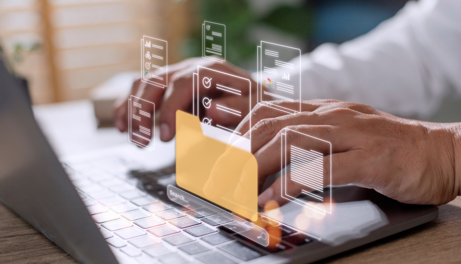 Cilvēks strādā pie klēpjdatora, kura tastatūras priekšā projicējas digitālas failu pārvaldības saskarne. Redzama dzeltena mape un apkārt tai caurspīdīgas dokumentu ikonas. Tas simbolizē datu meklēšanu un sakārtošanu digitālā vidē.