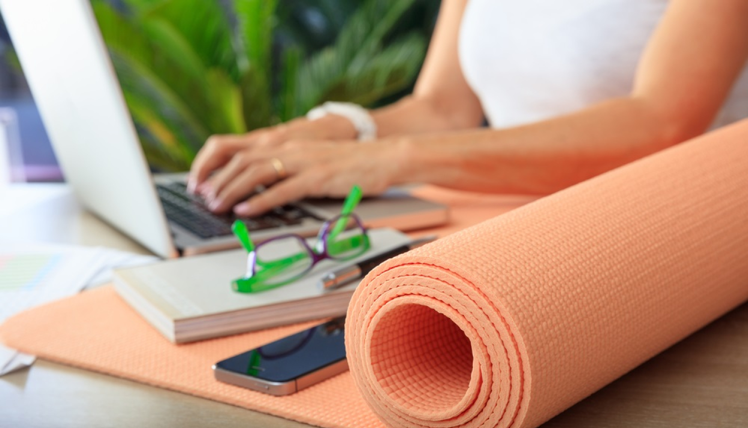 Sieviete pie datora. Uz galda vingrošanas paklājiņš. 