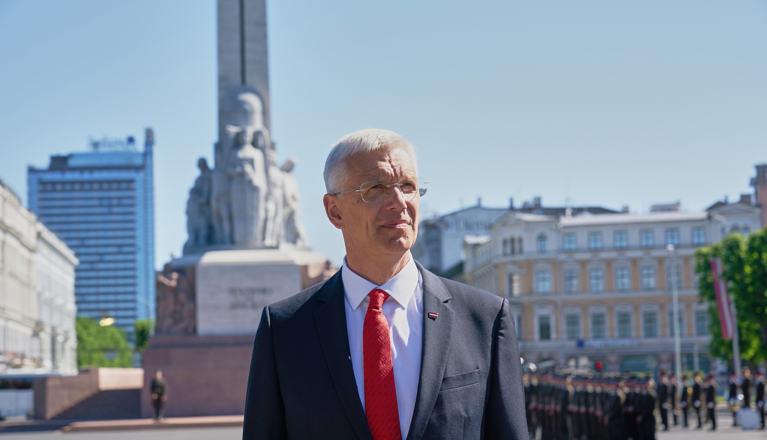 Ministru prezidents Krišjānis Kariņš uzvalkā un sarkanā šlipsē ar Brīvības pieminekli fonā