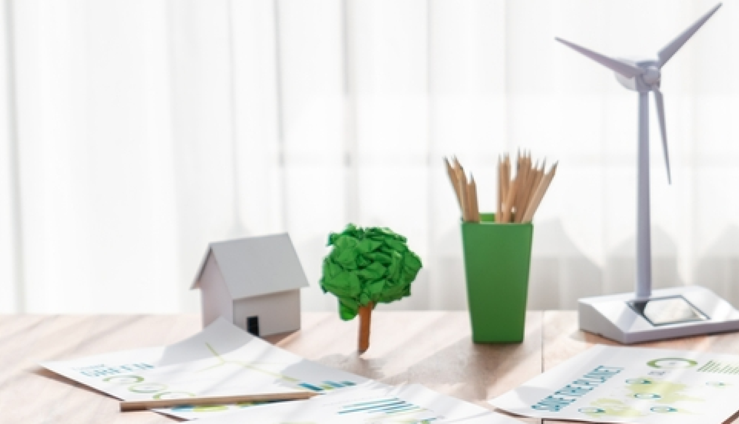 Uz galda dažādi priekšmeti, kas simbolizē zaļo enerģiju, piem, zaļs koks, vēja ģenerators 