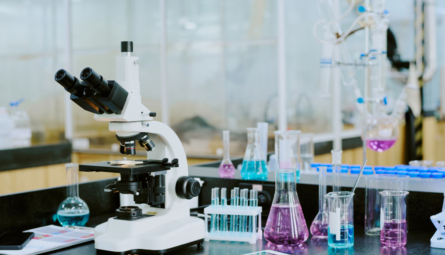 Mikroskops un mēģenes uz galda laboratorijā