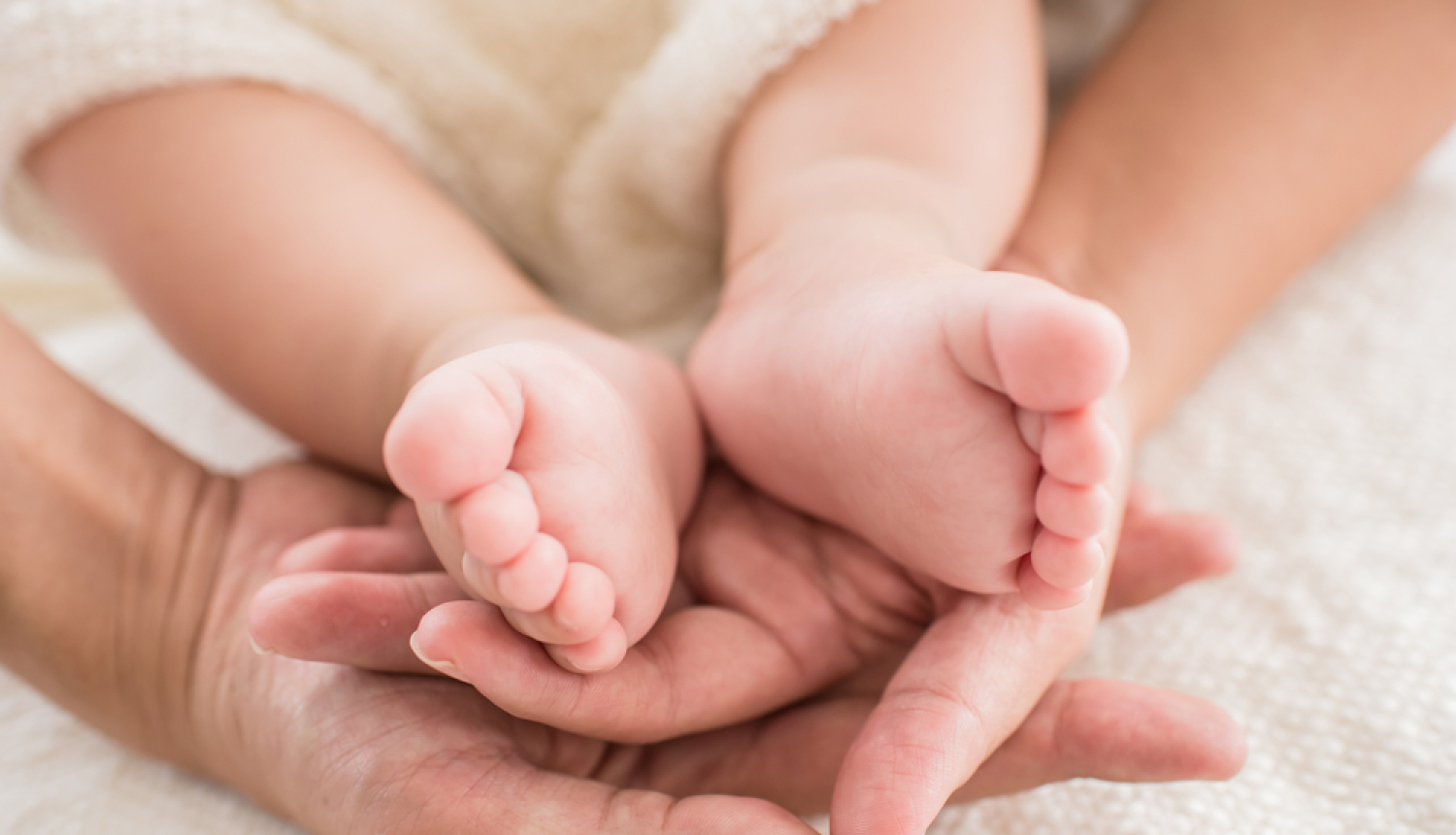 Pieaugušais tur rokās zīdaiņa kājas