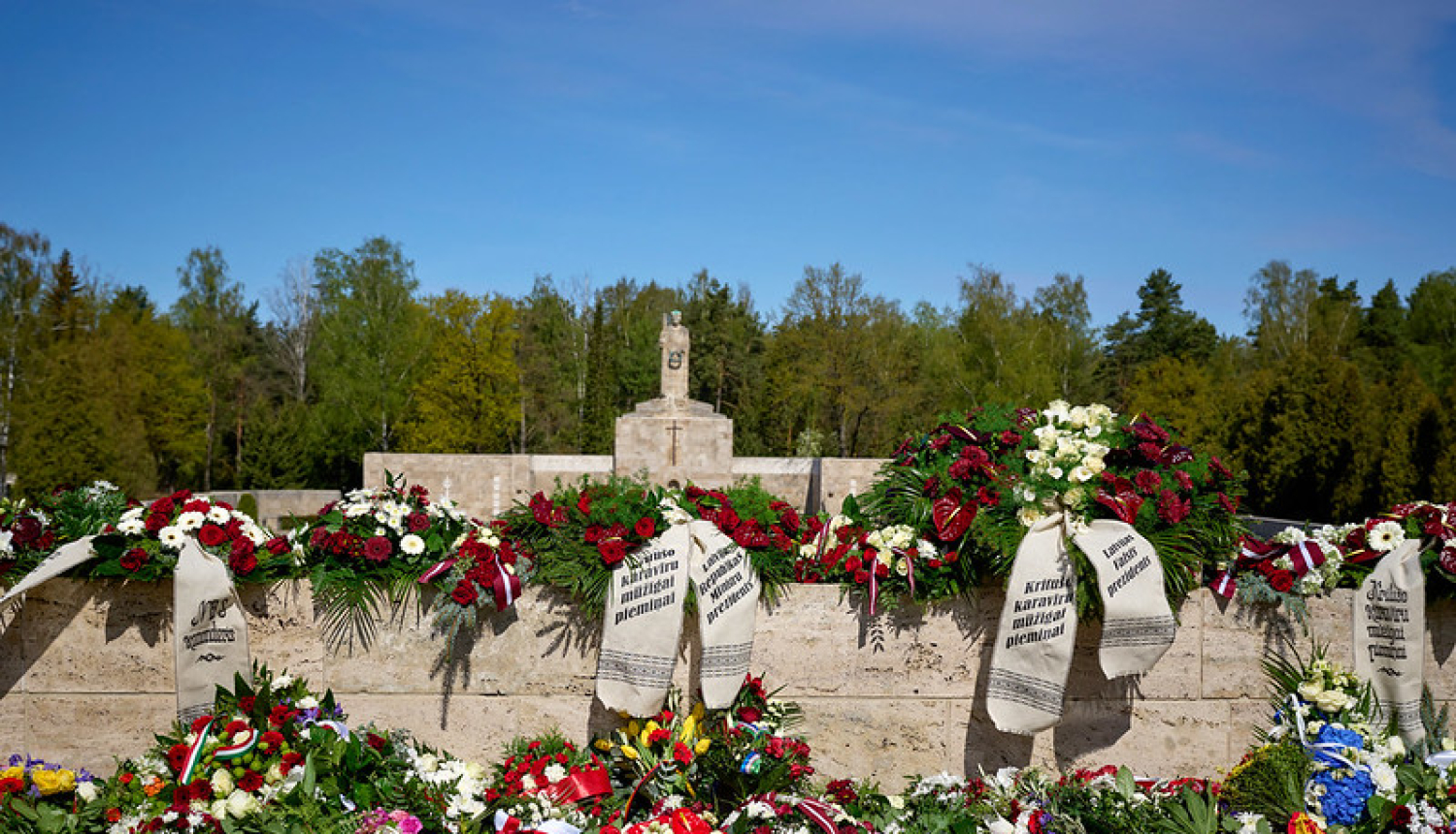 Brāļu kapu siena ar Māti Latviju. Ziedu vainagi ar lentām kritušo karavīru piemiņai. 