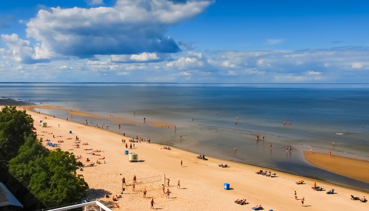 Skatās uz smilšu pludmali ar atpūtniekiem un jūru zem debesīm ar baltiem mākoņiem