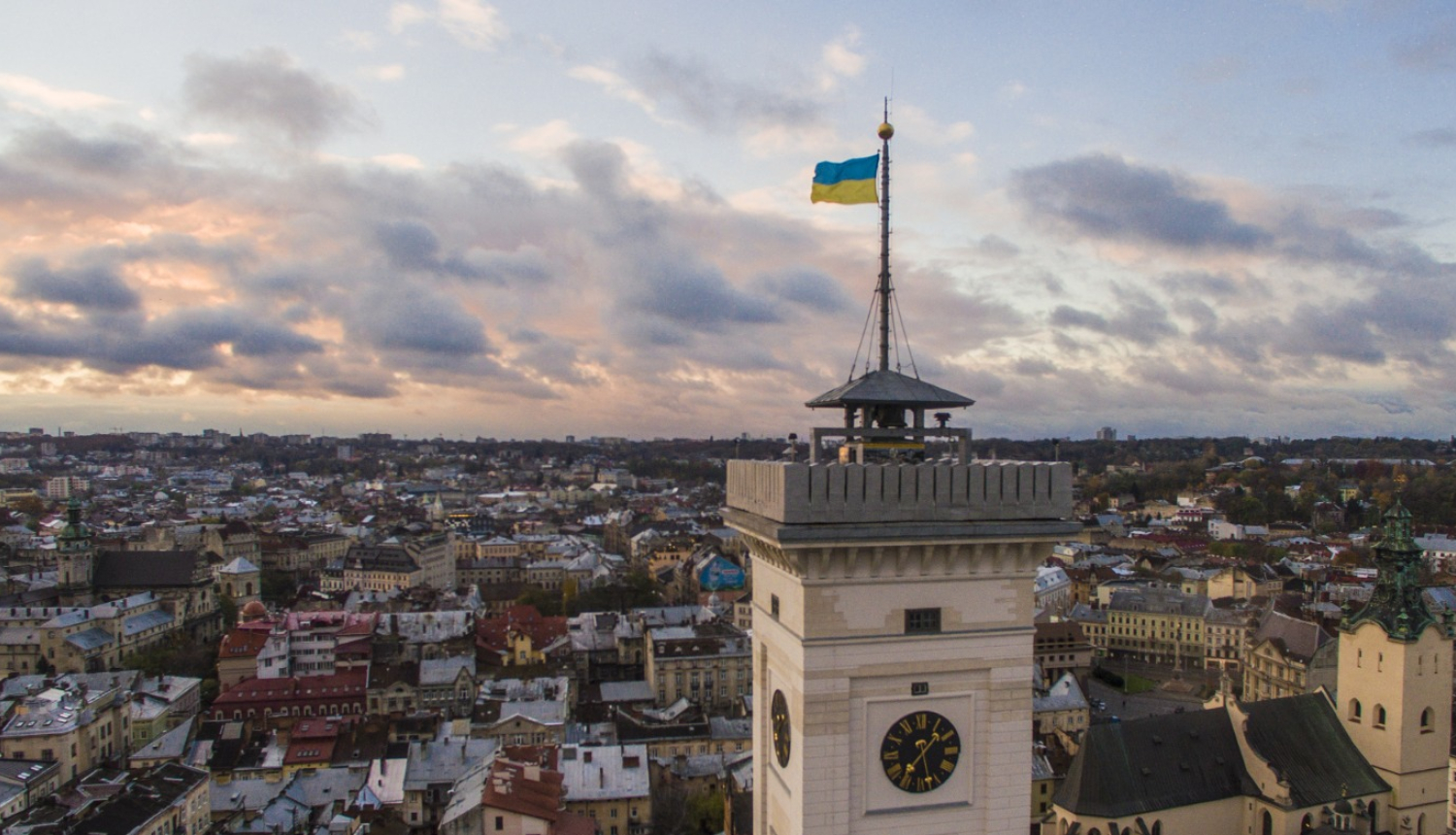 Skats no putna lidojumu pār Ukrainas pilsētu Ļvivu. Pirmajā plānā redzams pulksteņa tornis ar plīvojošu Ukrainas karogu