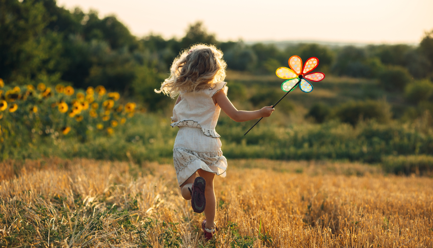 Bērns skrien pļavā, rokā krāsainas vējdzirnavas puķes formā