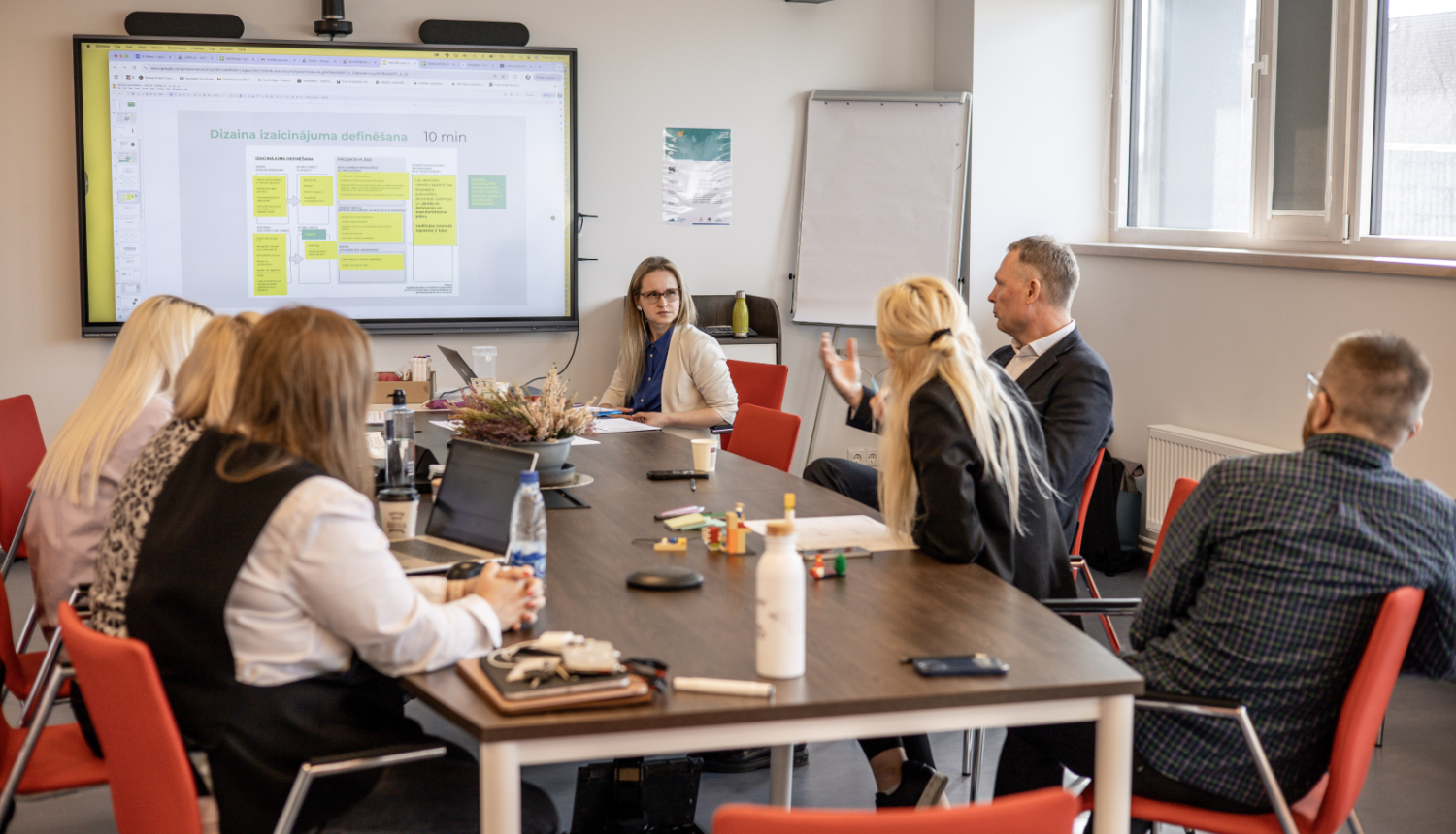 Inovāciju sprints - dalībnieki sēž pie galda, sarunājas un vēro ekrānu